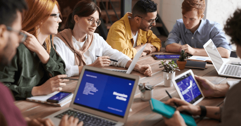 People gathering around a table with their laptops to work.