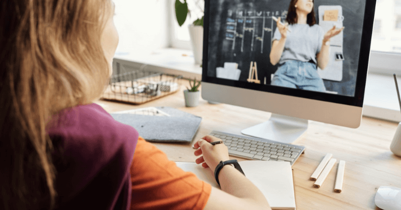 Woman taking notes watching training course on computer.